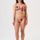 Bikini sostenible Gara Calei. Top con aros y tirantes ajustables, braga normal con lazadas. Tejido reciclado ECOWAVE® con estampado tie-dye y acabado lúrex. Hecho en España de forma ética.