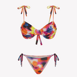 Bikini sostenible Gara Calei. Top con aros y tirantes ajustables, braga normal con lazadas. Tejido reciclado ECOWAVE® con estampado tie-dye y acabado lúrex. Hecho en España de forma ética.