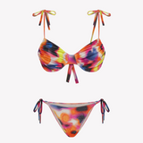 Bikini sostenible Gara Calei. Top con aros y tirantes ajustables, braga normal con lazadas. Tejido reciclado ECOWAVE® con estampado tie-dye y acabado lúrex. Hecho en España de forma ética.