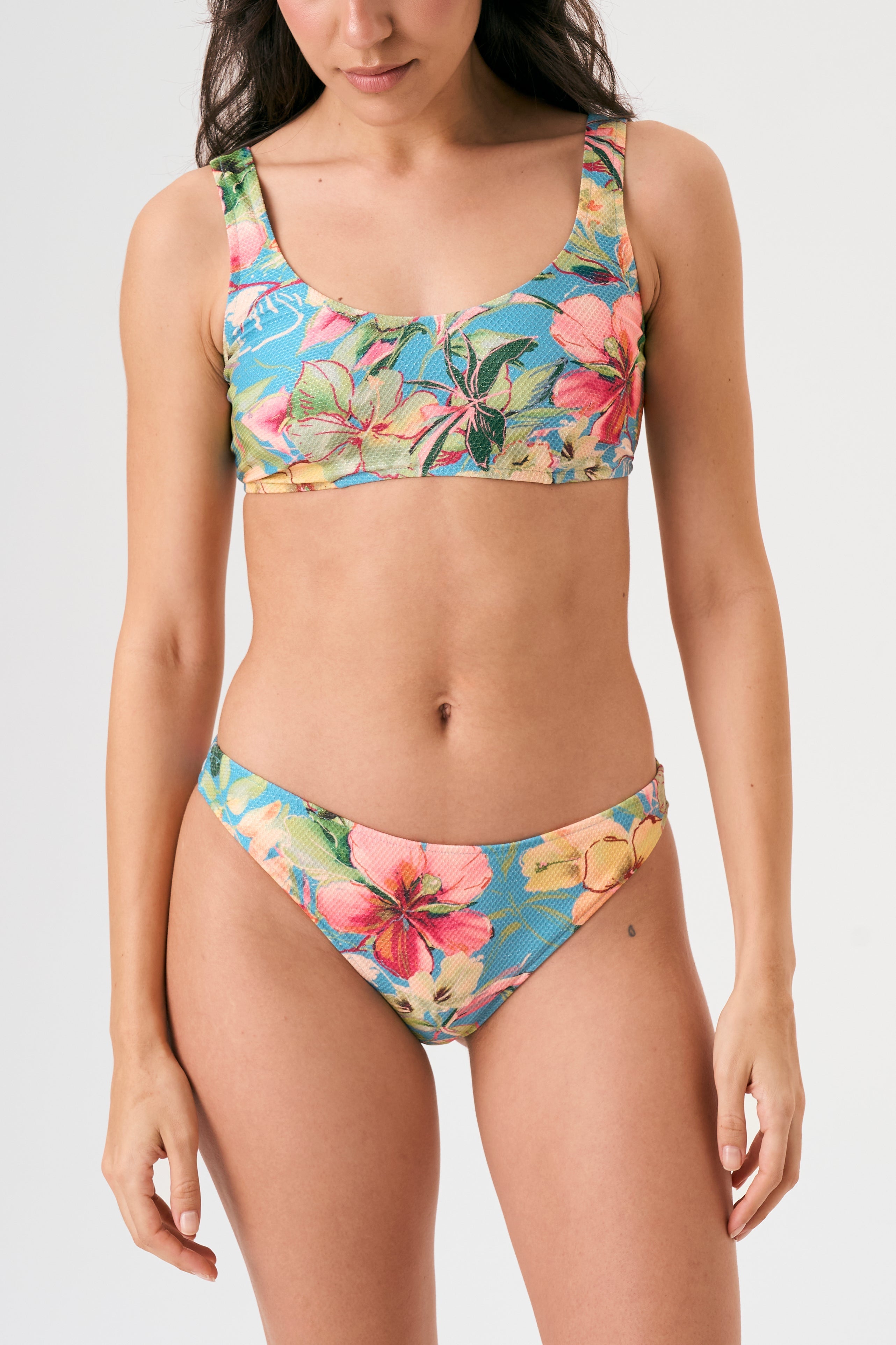 Bikini sostenible deportivo Mani Bimba Aloa. Top con tirantes anchos y sujeción óptima. Braguita de cobertura normal. Tejido reciclado ECOWAVE® con estampado floral en textura piqué y acabado lúrex. Hecho en España.