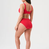 Bikini sostenible deportivo Mani Bimba Berry High. Top deportivo con tirantes anchos y braguita alta. Tejido reciclado ECONYL®. Color rojo cereza con textura atoallada. Hecho en España de forma ética. Ideal para máximo confort y sujeción.